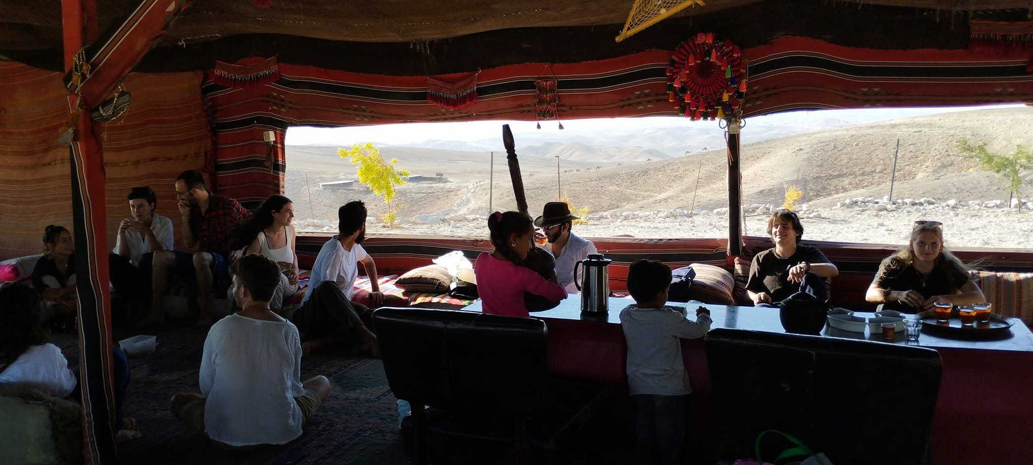 People gathered in a Bedouin tent workroom with desert hills outside