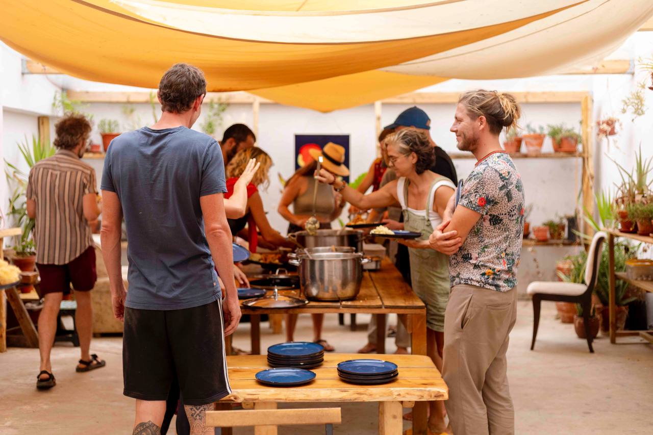 Community members serving and sharing a meal beneath a shaded canopy